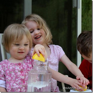 Emma squeezes a lemon and Lily pours the juice into the lemonade pitcher